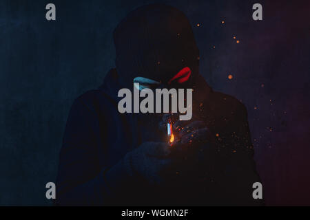 young man in hoodie and balaclava light a cigarette and looking down Stock Photo