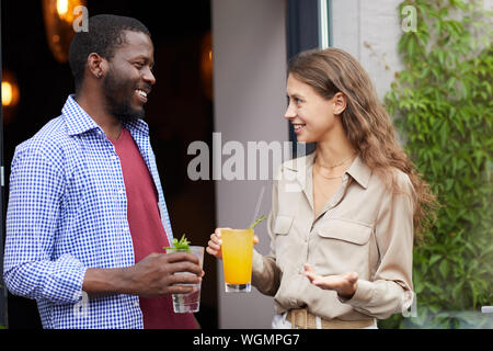 Waist up portrait of smiling young woman talking to African-American man outdoors, both holding cold refreshing drinks, copy space Stock Photo