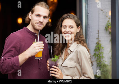 Waist up portrait of beautiful young couple drinking cocktails while posing outdoors standing by cafe, copy space Stock Photo
