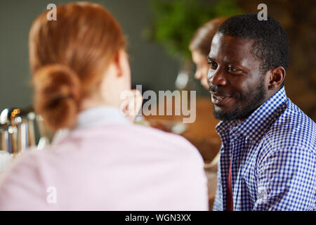 Portrait of African-American man talking to young woman while sitting with group of friends at table in cafe, copy space Stock Photo