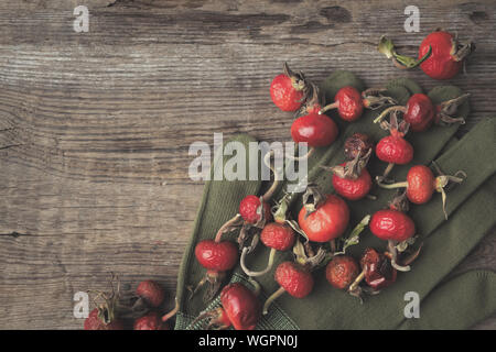 Rose hip berries, sweet briar fruits, gloves on wooden board. Top view. Stock Photo