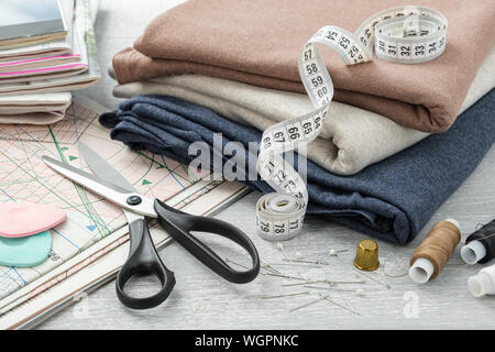 Sewing items: colorful fabrics, scissors, measuring tape, thimble, spools of threads, including pins, chalks, sewing pattern and magazines on a tablet Stock Photo