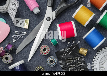 Sewing items: tailoring scissors, measuring tape, thimble, spools of thread, including pins, needles and sewing accessories on sewing cloth. View from Stock Photo
