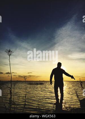Rear View Of Silhouette Man Holding Gun In Sea Against Sky During Sunset
