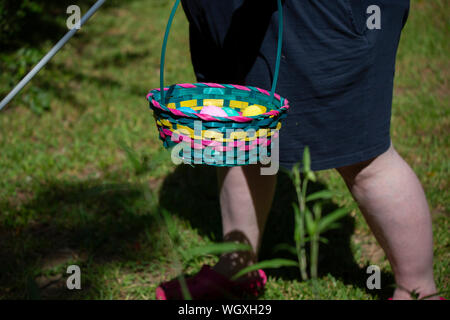 Blind woman carrying a cane and a colorful Easter basket filled with yellow, blue, green, purple, and pink eggs Stock Photo