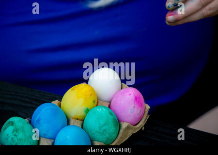 Plastic Easter eggs dyed green, blue, pink, and yellow in the carton with one undyed egg Stock Photo
