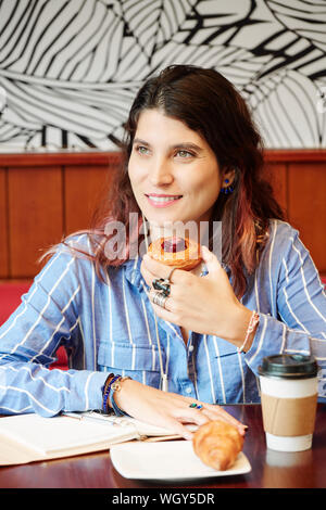 Portrait of pretty smiling young Caucasian woman eating delicious pastry for dessert in cafe Stock Photo
