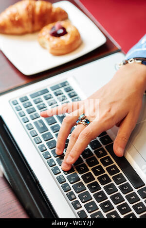 Close-up image of female software developer sitting at table in bakery and working on laptop, view from above Stock Photo