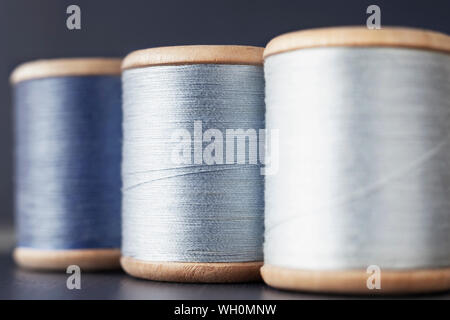 Three wooden spools of colored thread on  colored background , different shades of blue color  in every spool Stock Photo