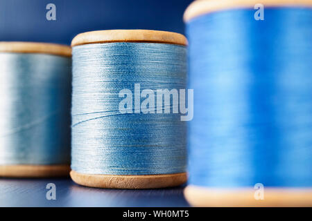 Three wooden spools of colored thread on  colored background , different shades of blue color  in every spool Stock Photo