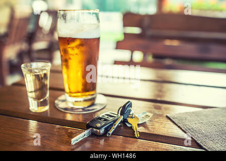 Car keys and glass of beer or distillate alcohol on table in pub or restaurant