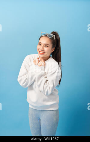 Happy woman keeps hands under chin looks joyfully at camera, notices something very pleasant, isolated over light blue background Stock Photo