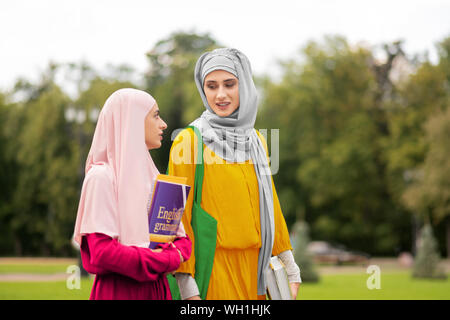 Muslim student wearing yellow dress talking to friend Stock Photo