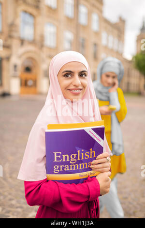 Beaming dark-eyed muslim woman holding English book Stock Photo