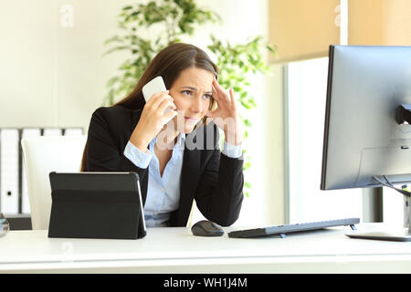 Worried office worker using multiple devices calling on phone at workplece Stock Photo