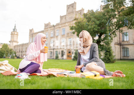Muslim students eating and drinking while sitting on lawn Stock Photo