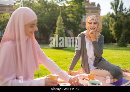 Muslim woman eating strawberry while having lunch with friend Stock Photo