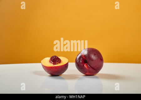 Two beautiful, ripe, juicy nectarines lie on a white table behind a yellow background. One fruit is cut and it has a bone Stock Photo