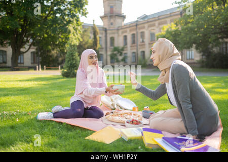 Students wearing hijabs eating pizza and fruits outside Stock Photo