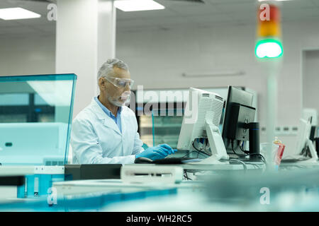 Concentrated mature scientist staring at screen of computer Stock Photo