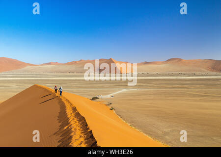 Two hikers walking on the ridge of Dune 45 in the morning light, Namib desert, Namibia Stock Photo