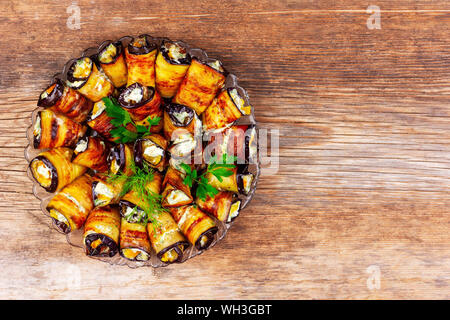 rolls of fried eggplant with sprigs of parsley and dill stuffed with tomatoes, mayonnaise and garlic on a wooden background closeup top view Stock Photo