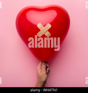 First aid with patch to wounded heart in woman hand on pink Stock Photo