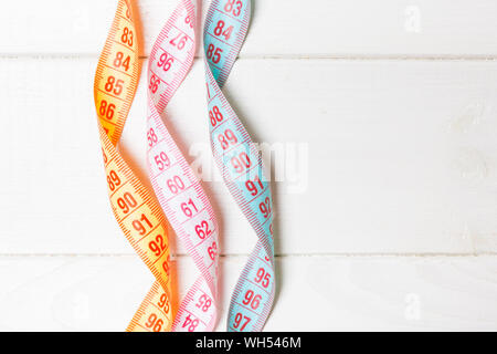 Top view of spiral colorful measure tapes on wooden background. Concept of perfect female figure with empty space for your idea. Stock Photo