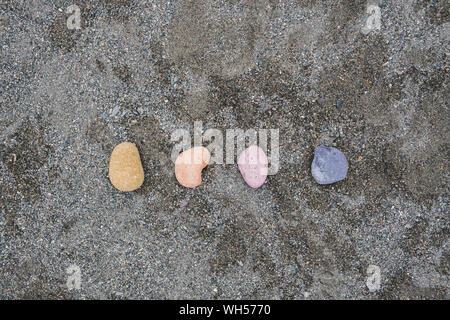 Multi-colored pebbles on wet gray sand. Yellow, orange, pink and purple pebbles on the sea beach, concept of naturalness, simplicity and beauty of nat Stock Photo