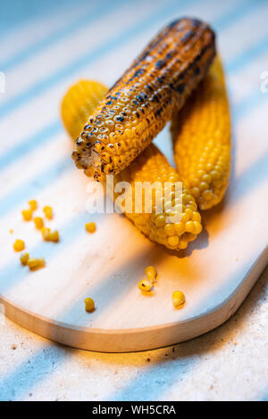 Fresh roasted or grilled corn cobs on a wooden chopping board. Stock Photo