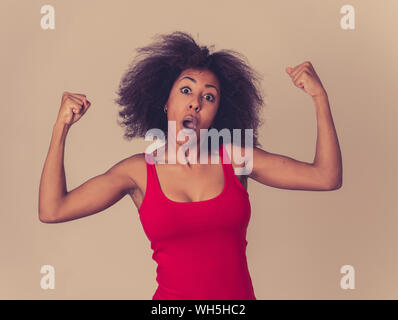 Portrait of young beautiful funny african american woman with afro hair style showing arms muscles smiling proud having fun. In people Success and Hap Stock Photo