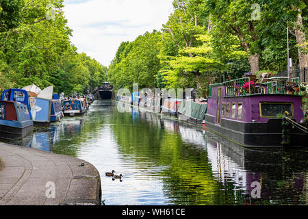 Colourful Narrow Boats Moored in Little Venice from Beneath the Warwick Avenue Road Bridge Over the Grand Union Canal With Watery Tree Reflections. Stock Photo