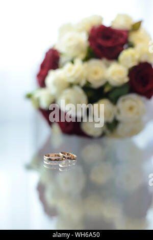 Gold wedding rings lie on a glass table next to the bouquet Stock Photo