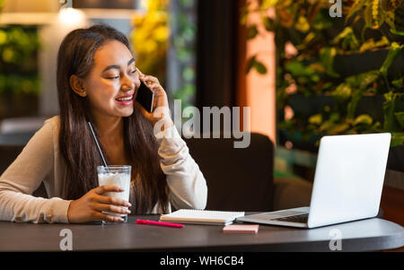 Cheerful teen girl talking on cellphone at cafe Stock Photo