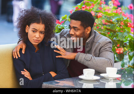 Cheerful black guy trying to cheer up his angry girlfriend Stock Photo