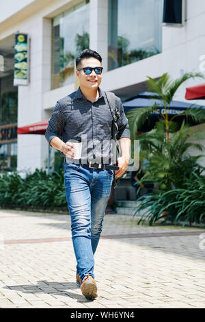 Cheerful handsome young man walking in the street with cup of take away coffee in hand Stock Photo
