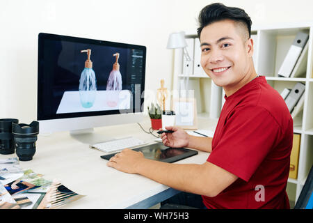 Cheerful young Vietnamese professional 3D designer working on graphic tablet on visualization for commercial project Stock Photo