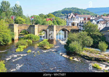 Hazy summer day in Llangollen, Wales. Flags flyalong the old stone bridge over the River Dee. Stock Photo