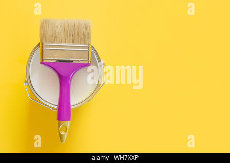 Purple brush with open can of white paint on yellow background. Trend repairs concept. Top view. Stock Photo