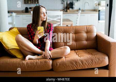 Young woman with cell phone on a couch at home Stock Photo