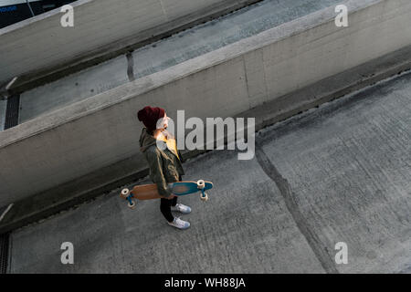 Stylish young woman with skateboard standing on parking deck Stock Photo