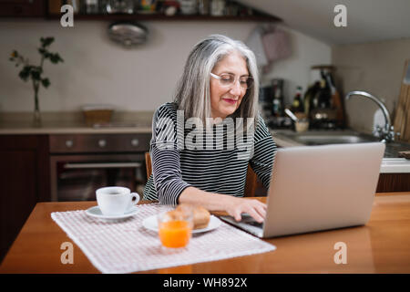 Portrait of senior woman using laptop at breakfast table Stock Photo