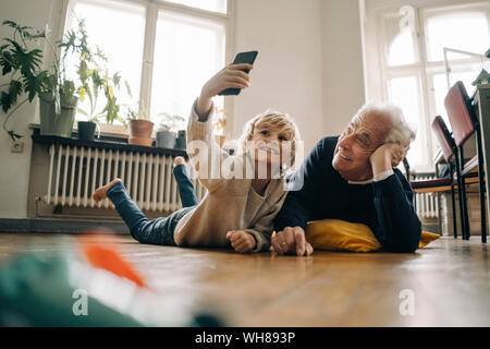Grandfather and grandson lying on the floor at home taking a selfie Stock Photo