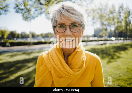 Portrait of smiling mature woman with grey hair wearing glasses and yellow clothes Stock Photo
