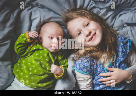 Portrait of smiling little girl lying on bed beside baby girl, top view Stock Photo