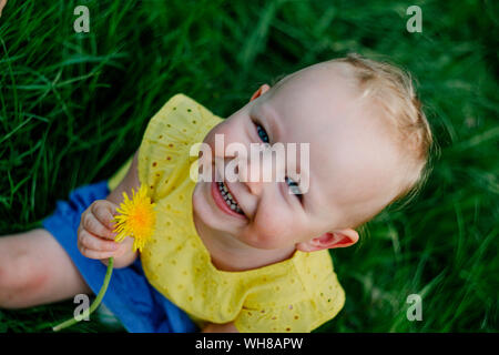 Portrait of happy little girl with dandelion sitting on a meadow Stock Photo