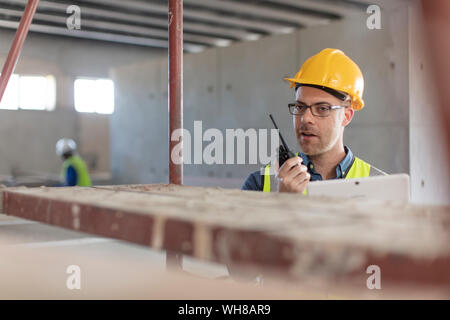 Architect using walkie talkie and laptop at construction site Stock Photo