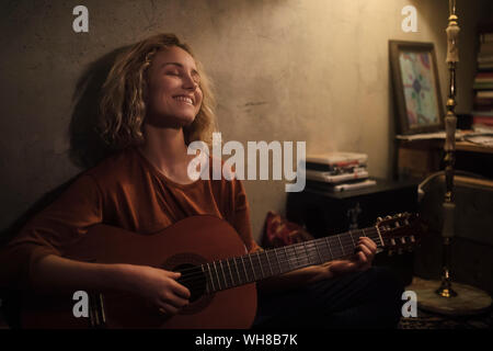 Happy young woman playing guitar at home Stock Photo