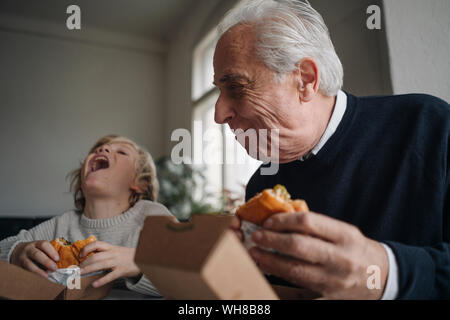 Happy grandfather and grandson eating burger together at home Stock Photo