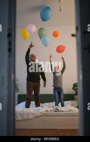 Happy grandfather and grandson playing with balloons on bed at home Stock Photo